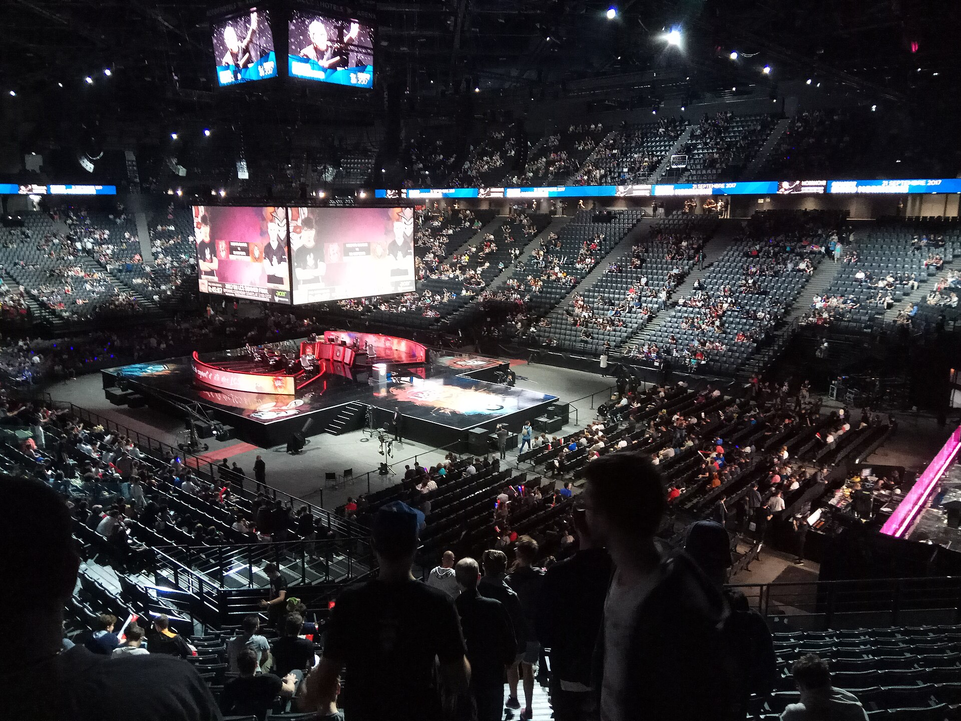 Une arène d'esport plongée dans la pénombre, avec la scène éclairée et le public dans les gradins