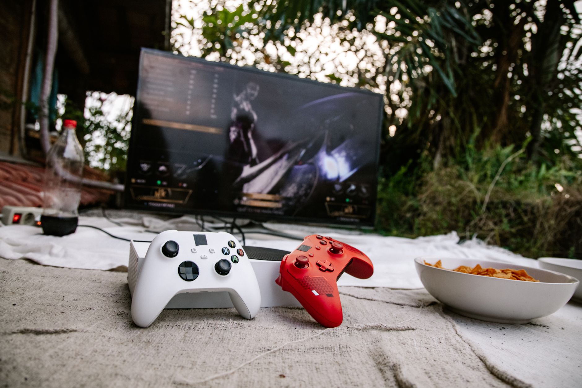 Une console de jeux blanche avec deux manettes devant un écran affichant un jeu vidéo en extérieur.
